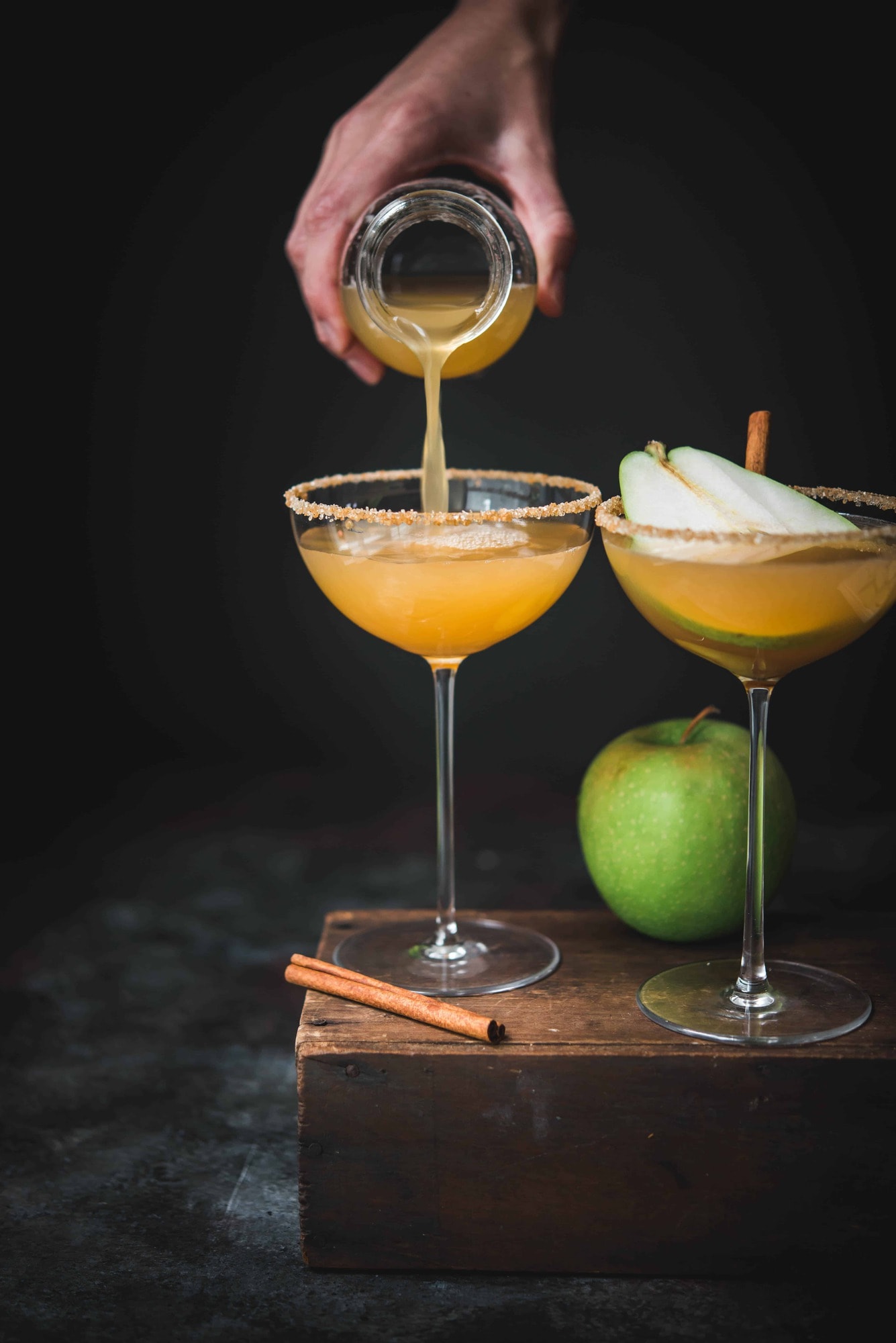 Pouring an apple cider pear martini into long-stemmed coupe glass with dark moody backdrop