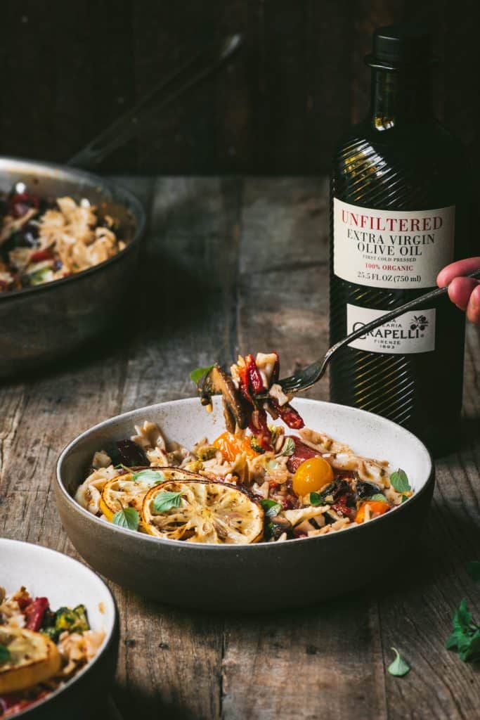 Side view of mediterranean pasta on a fork with bottle of olive oil in background