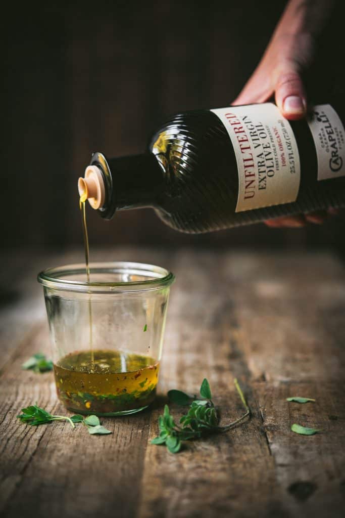 Pouring Carapelli olive oil into glass jar filled with herbs
