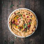 Overhead of roasted carrot eggplant dip in a white bowl, garnished with pomegranate and fresh herbs