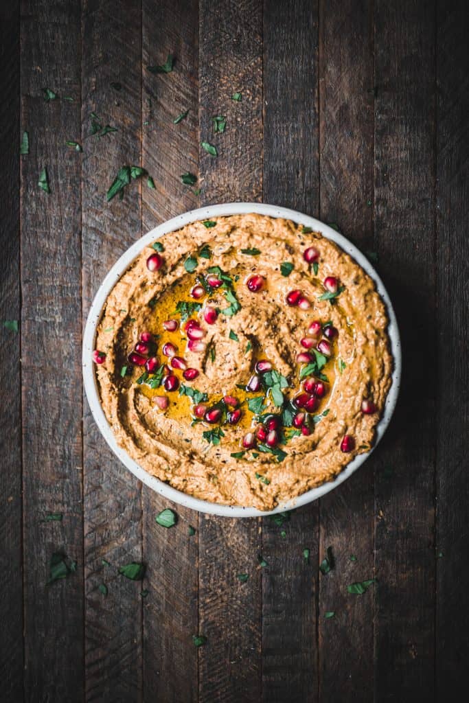 Overhead of roasted carrot eggplant dip in a white bowl, garnished with pomegranate and fresh herbs