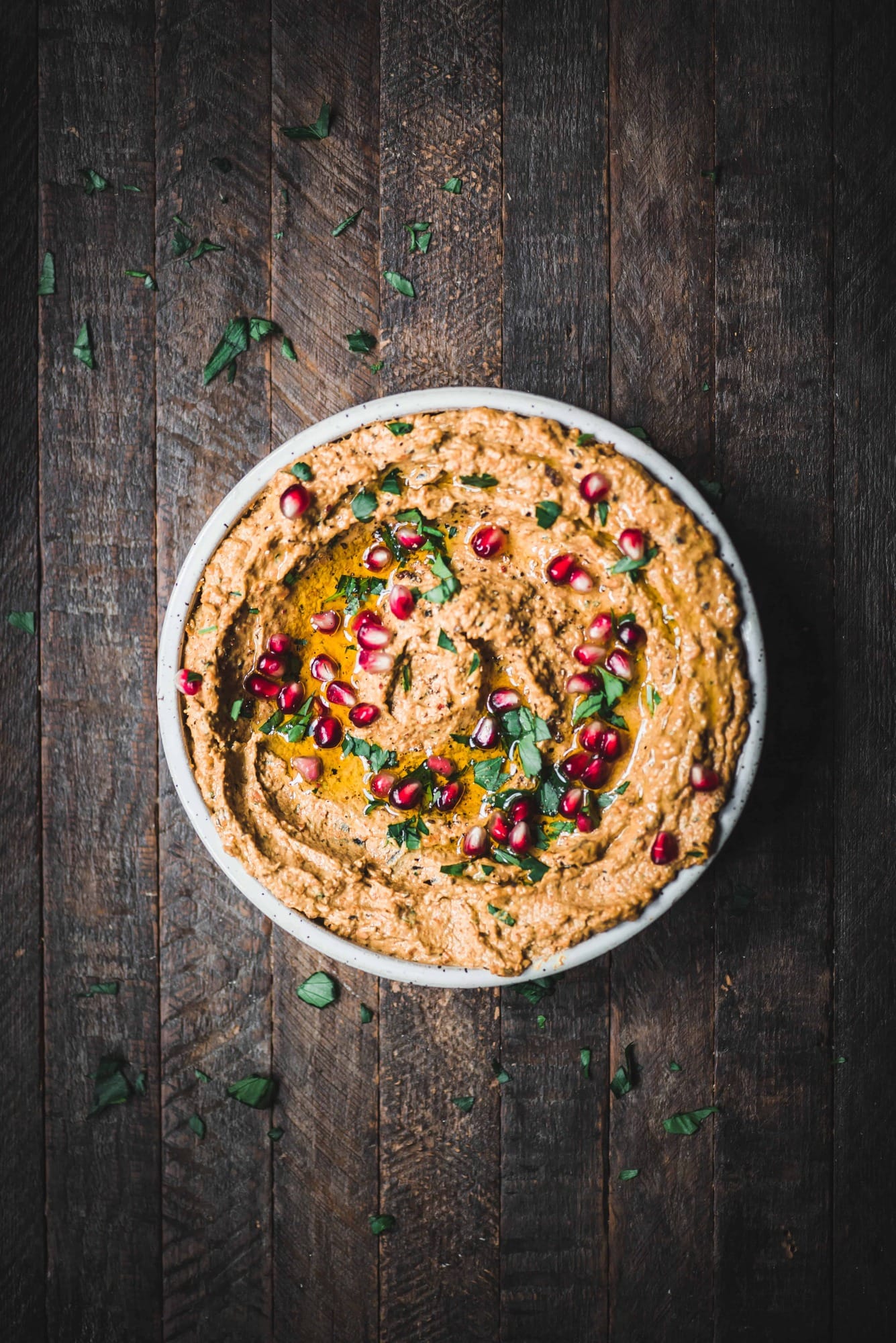 Overhead of roasted carrot eggplant dip in a white bowl, garnished with pomegranate and fresh herbs