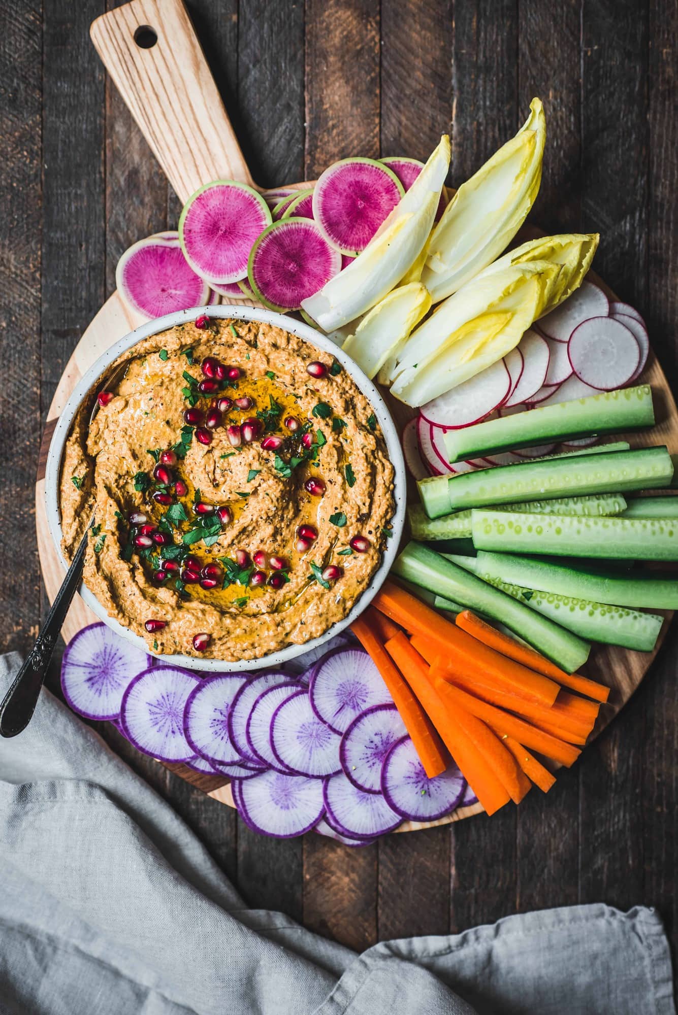 Overhead of roasted carrot eggplant dip in a white bowl surrounded by colorful vegetables on a circular platter