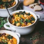 45 degree angle of fall vegetable minestrone in a white bowl on a rustic wood background.