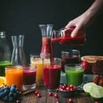 Side view of glasses and carafes of fresh fall juices, hand pouring juice into glass