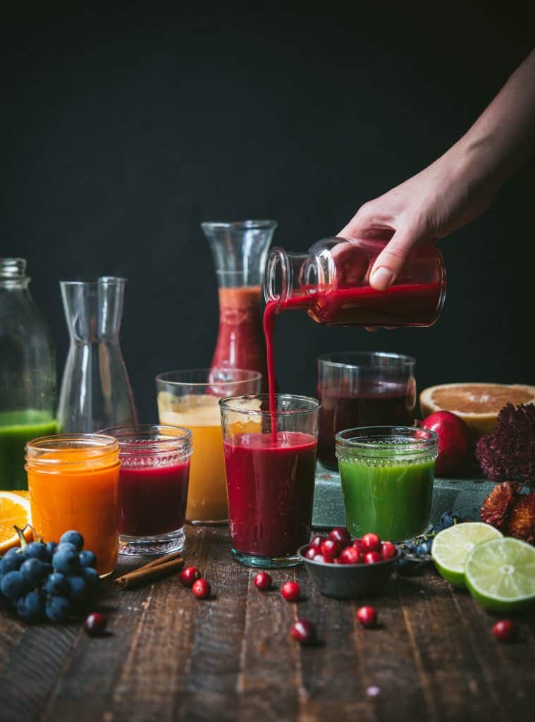Side view of glasses and carafes of fresh fall juices, hand pouring juice into glass