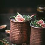 Side view of fig moscow mule vodka cocktail in copper mug with cinnamon sticks and fresh thyme