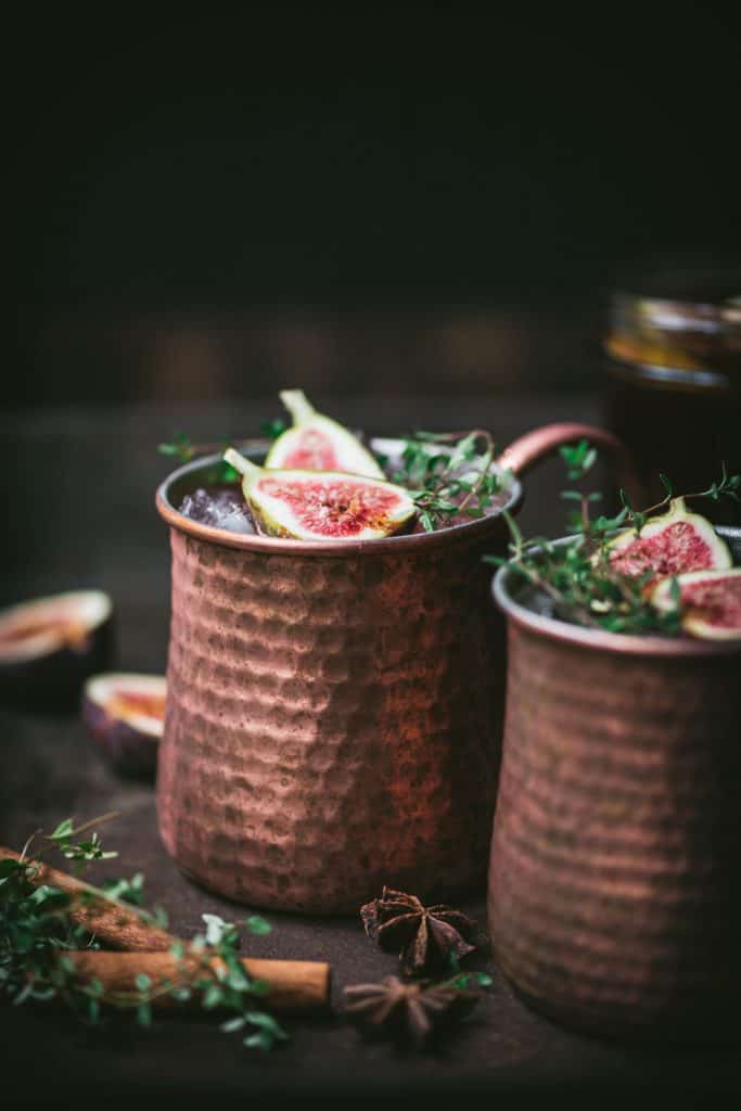 Side view of fig moscow mule in copper mug with cinnamon sticks and fresh thyme