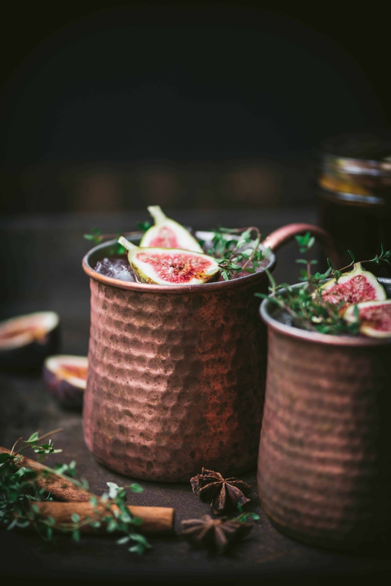 Side view of fig moscow mule vodka cocktail in copper mug with cinnamon sticks and fresh thyme