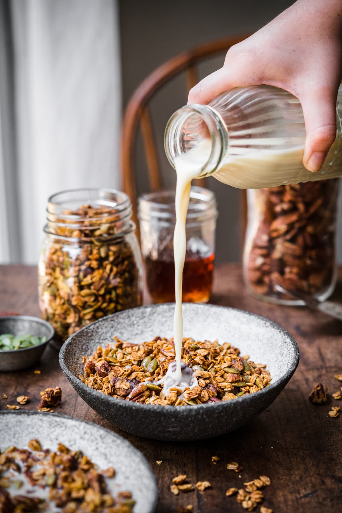 Pouring milk into a bowl of pumpkin spice granola on wood table.