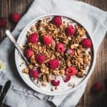 Overhead of pumpkin spice granola with milk and fresh raspberries in a white bowl