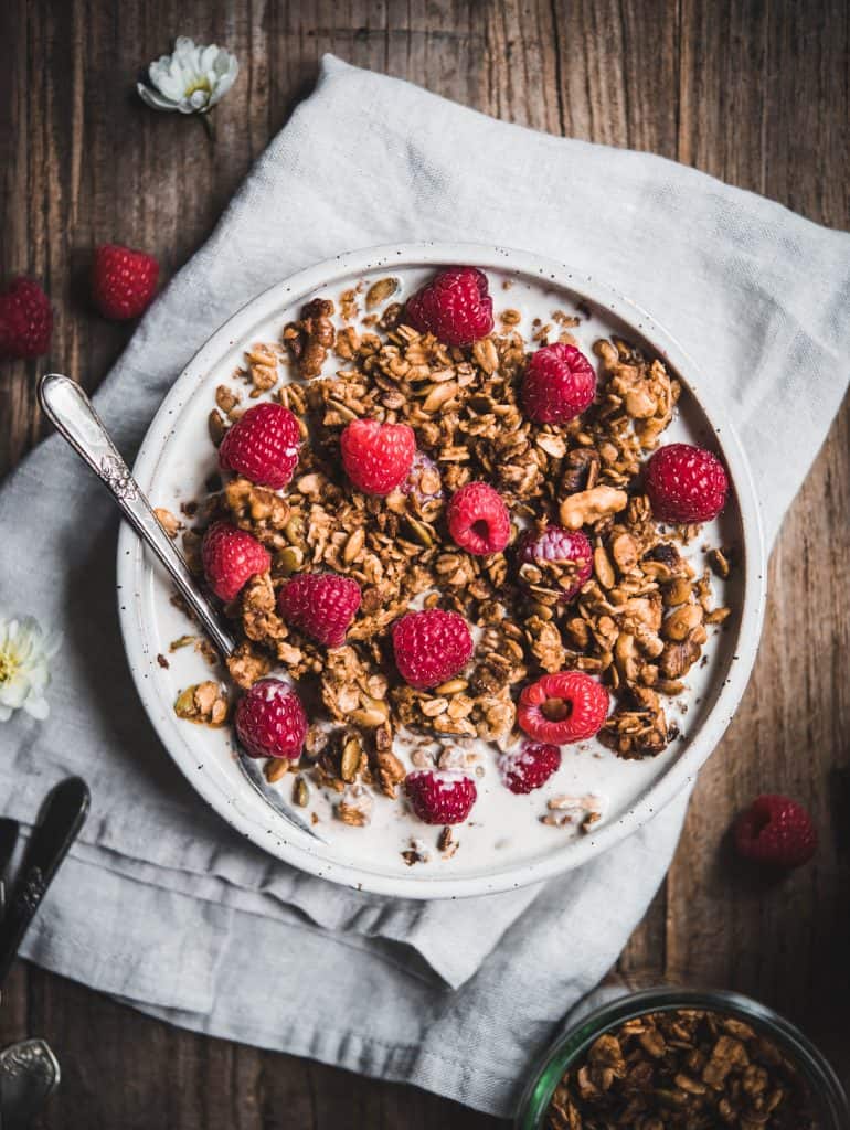 Overhead of granola with milk and fresh raspberries in a white bowl