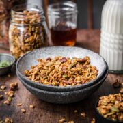 Front view of a bowl of granola with granola and milk in the background.