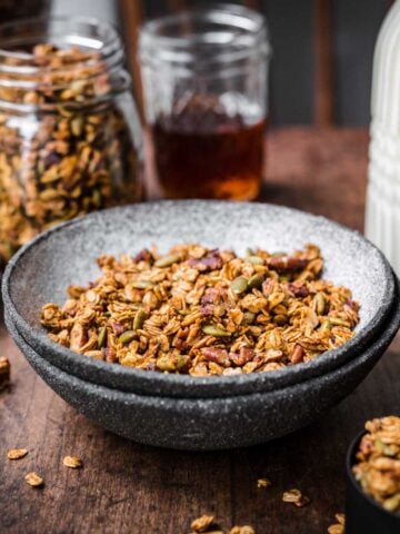 Front view of a bowl of granola with granola and milk in the background.