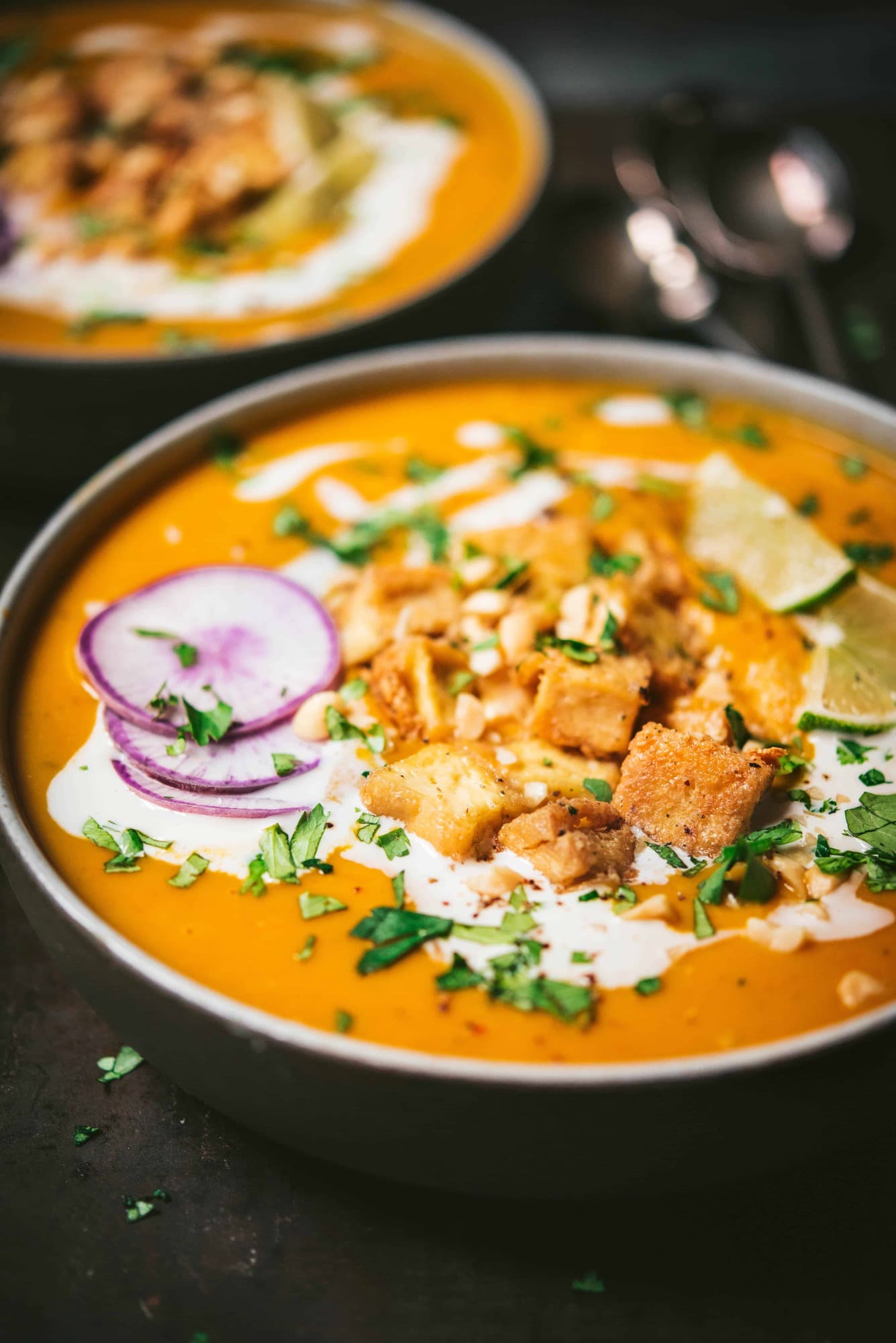 Close up side view of thai red curry pumpkin soup with crispy tofu in a black bowl