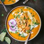 Overhead of thai red curry pumpkin soup in black bowl garnished with crispy tofu, lime, fresh herbs and purple daikon radish