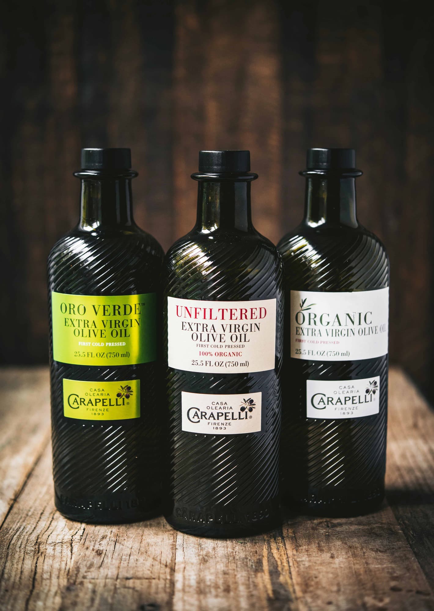 Three bottles of Carapelli Olive Oil on rustic wood background
