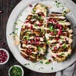 Stuffed roasted eggplants drizzled with tahini and pomegranate on a white plate