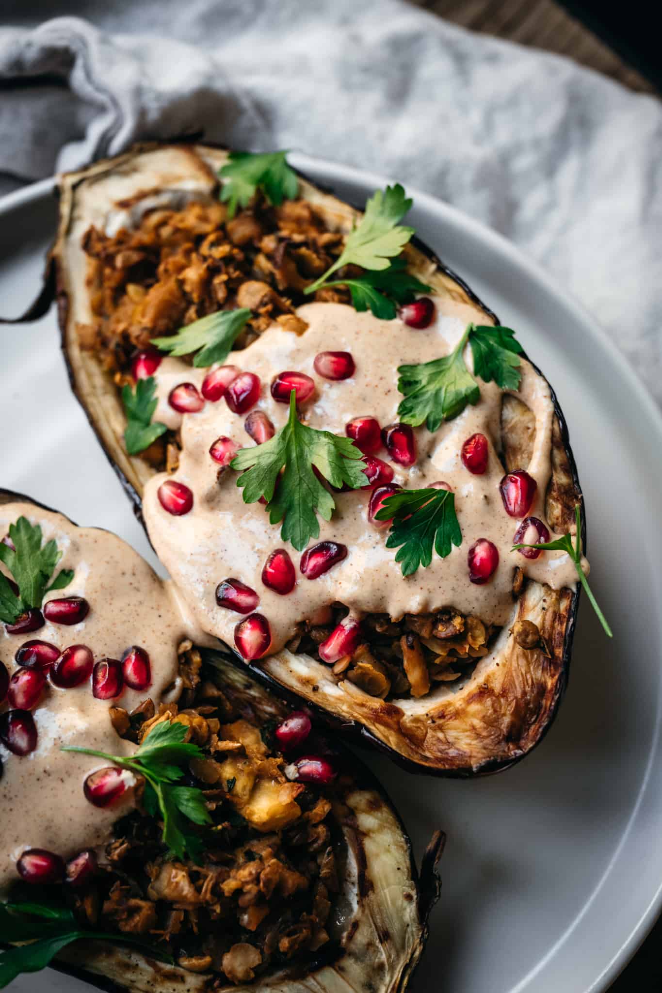 Side view of Stuffed roasted eggplants drizzled with tahini and pomegranate on a white plate