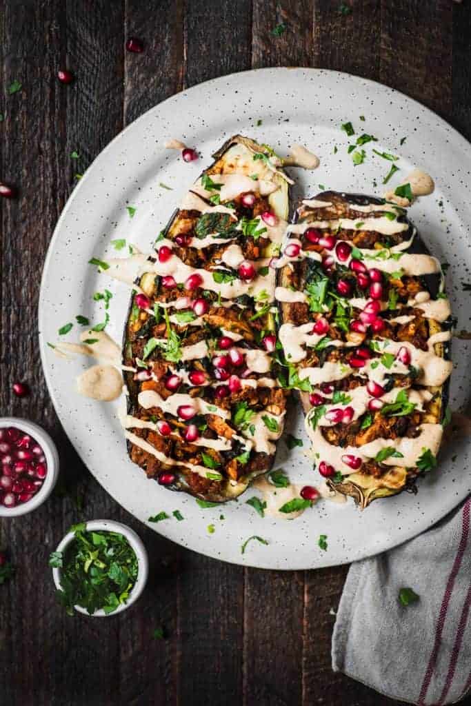 Stuffed roasted eggplants drizzled with tahini and pomegranate on a white plate
