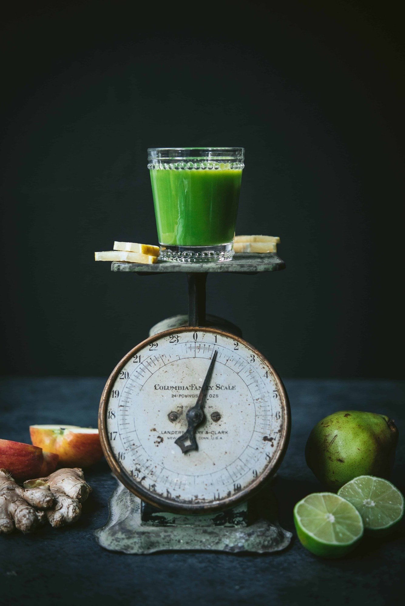 Small glass of green juice atop an antique green scale