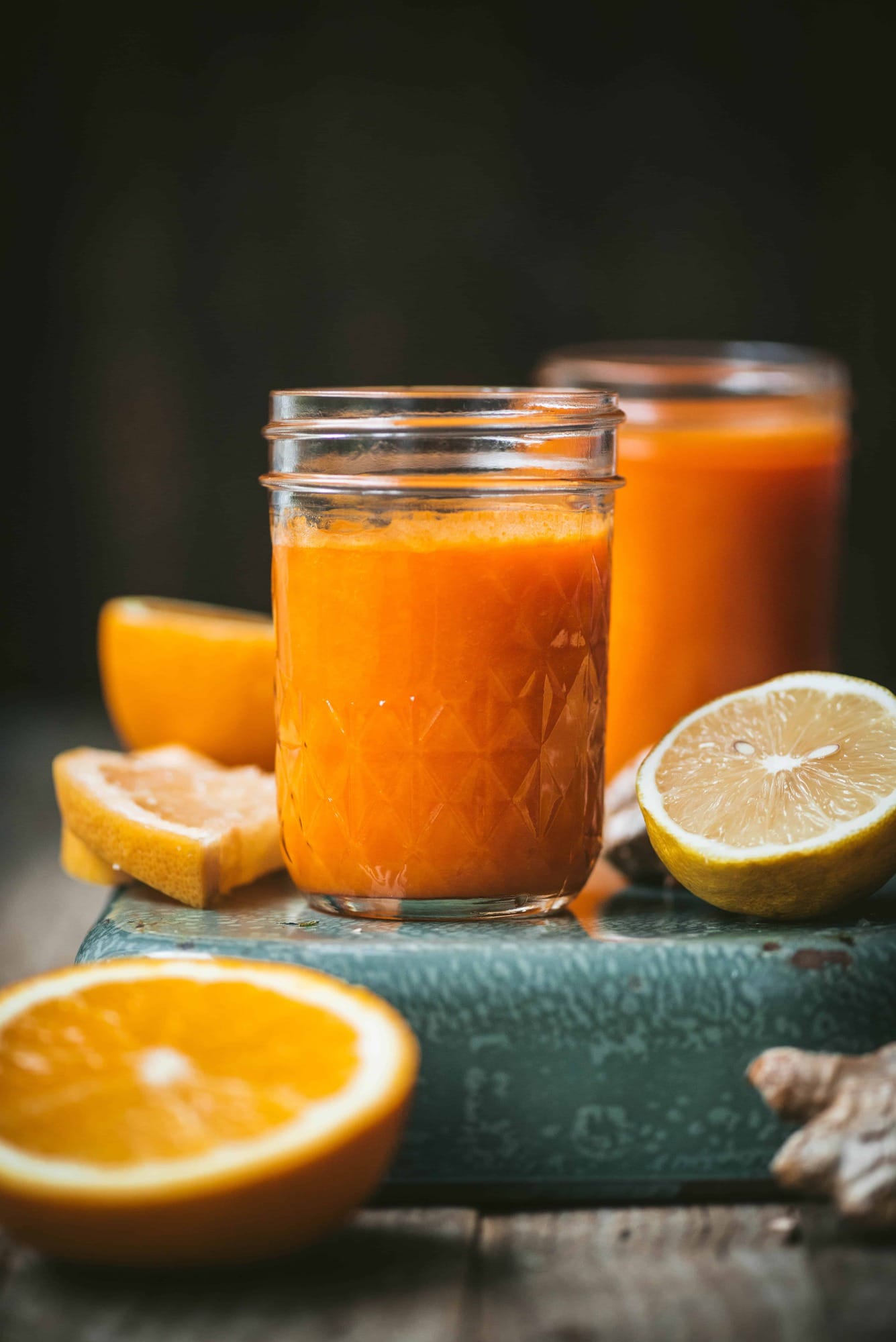 Close up of homemade orange juice with fresh lemons and oranges on a teal background