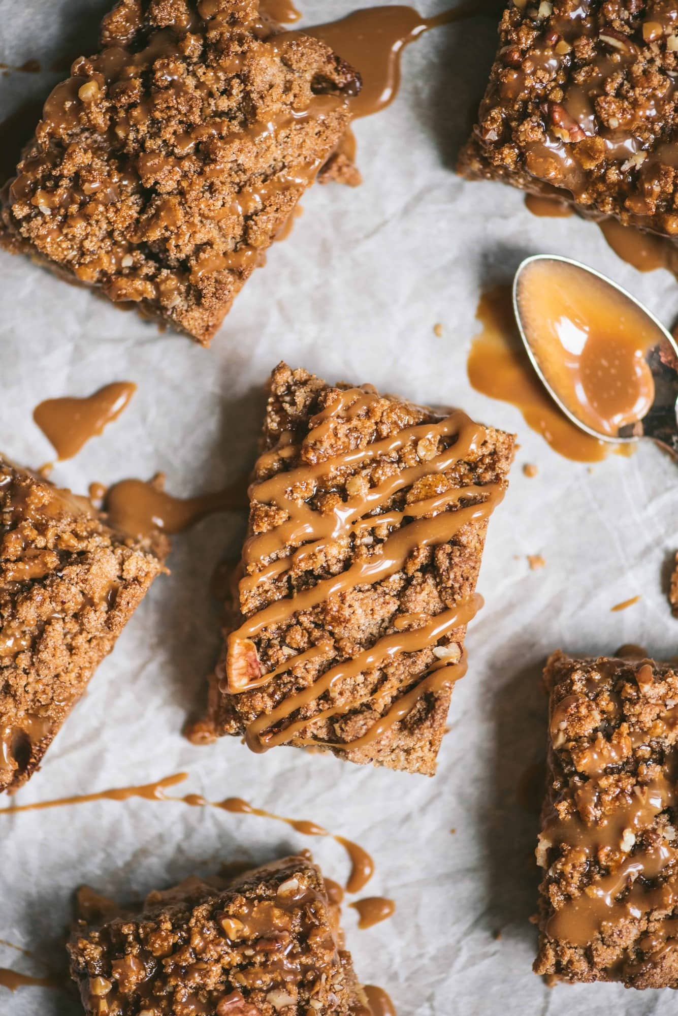 Overhead of vegan apple pie crumble bars drizzled with caramel on parchment paper