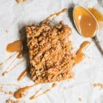 Overhead of vegan apple pie crumble bar drizzled with caramel on parchment paper