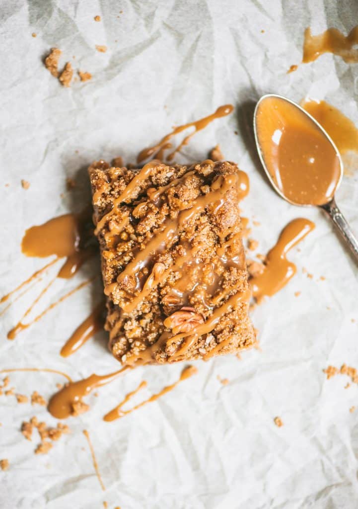 Overhead of vegan apple pie crumble bar drizzled with caramel on parchment paper