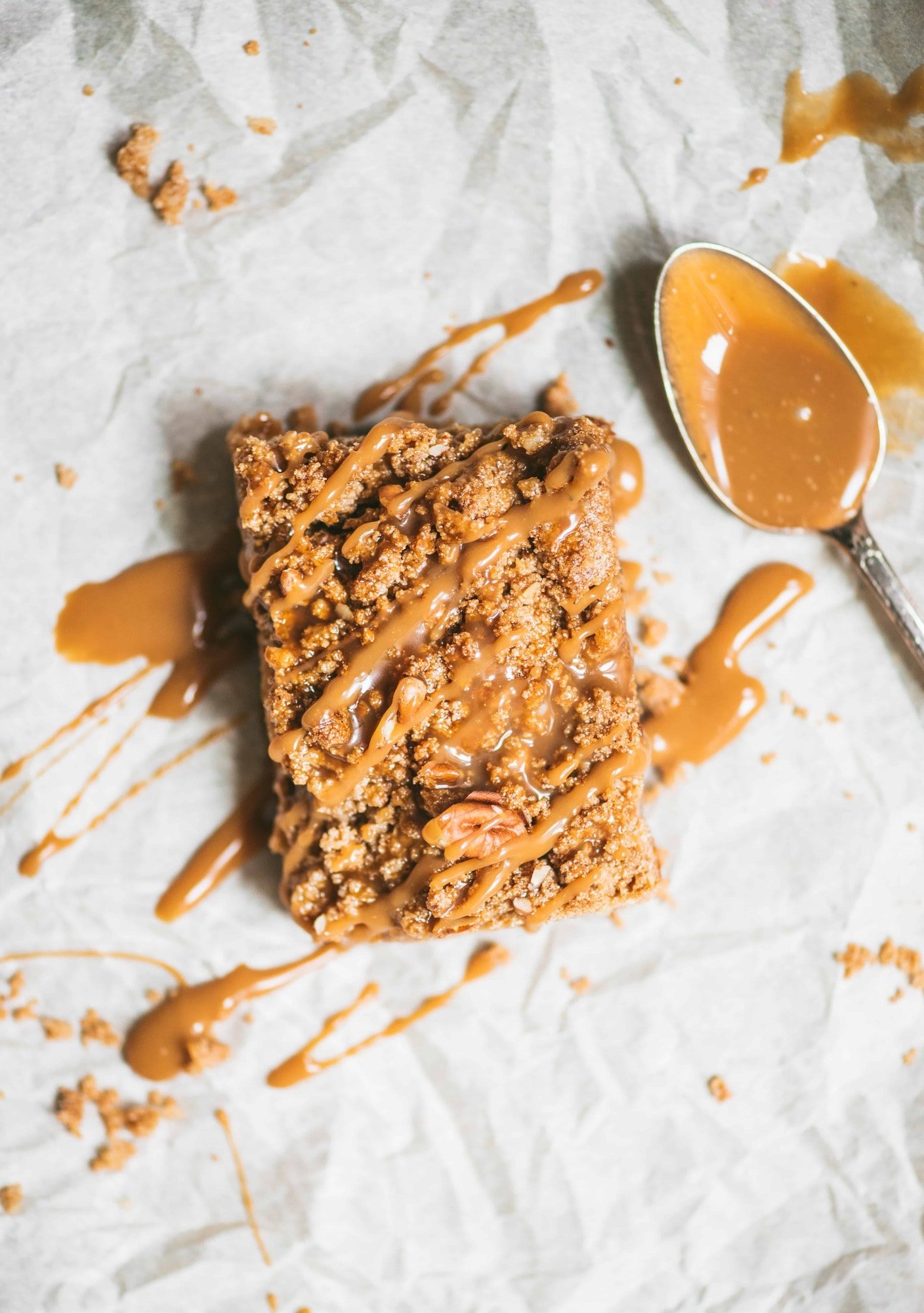 Overhead of vegan apple pie crumble bar drizzled with caramel on parchment paper