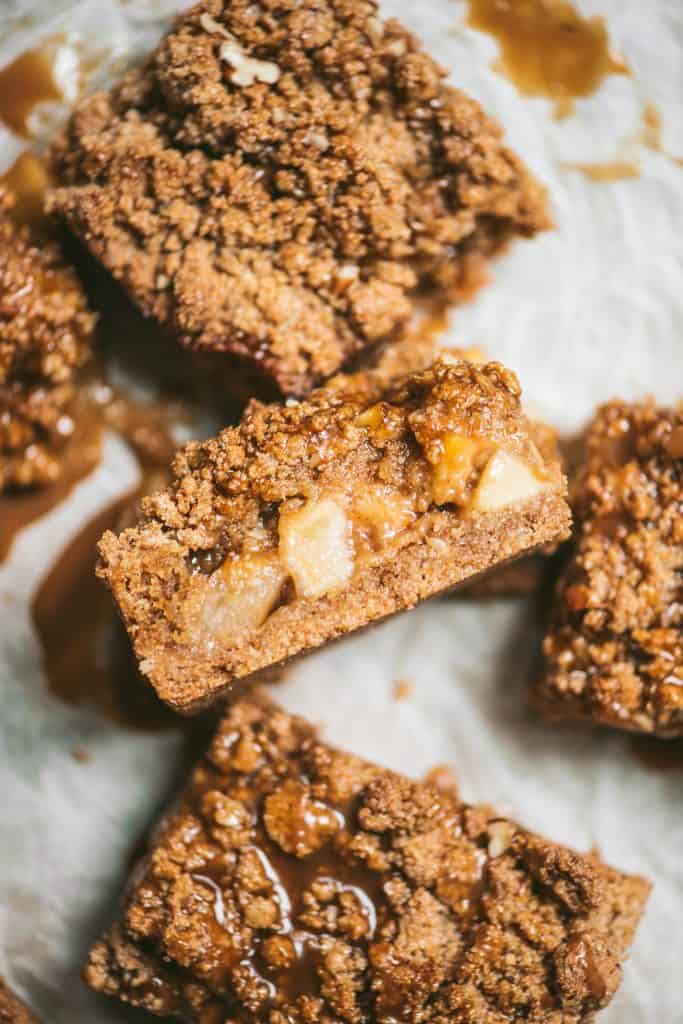 Side view of a caramel apple pie crumble bar on white parchment paper