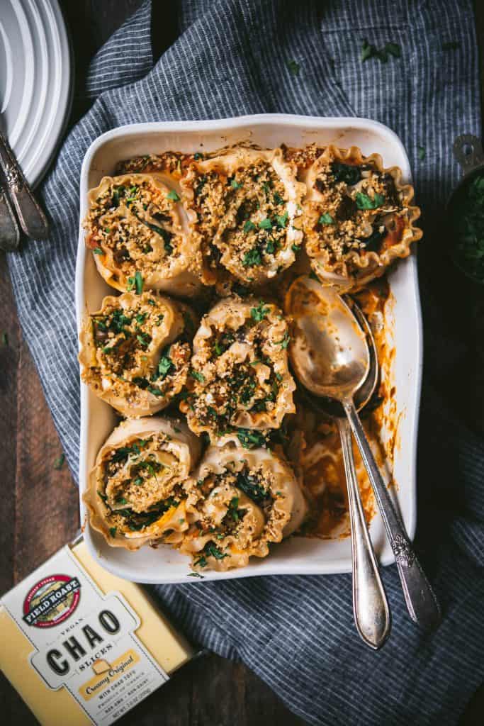Overhead of vegan butternut squash lasagna roll ups in a white pan with two spoons and Chao vegan cheese