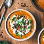 Overhead of crushed lentil soup in a white bowl garnished with cream, lentils and herbs