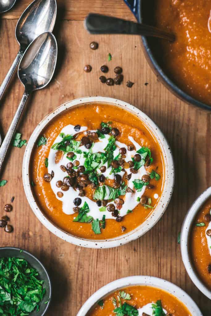 Overhead of crushed lentil soup in a white bowl garnished with cream, lentils and herbs