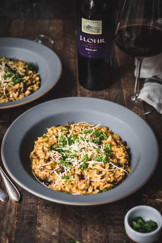 Side angle of wild mushroom risotto in gray bowl served with red wine