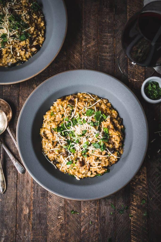 Overhead of wild mushroom risotto in gray bowl served with red wine