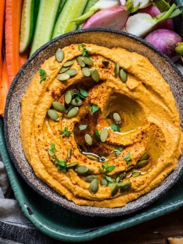 Overhead view of pumpkin hummus in a bowl garnished with pumpkin seeds.