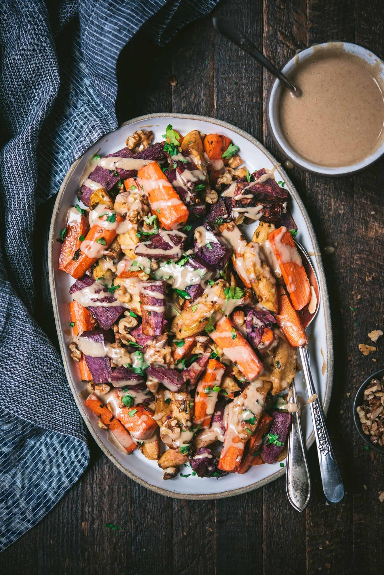 Roast carrots, purple potatoes and apples with cinnamon tahini on a white tray with blue linen