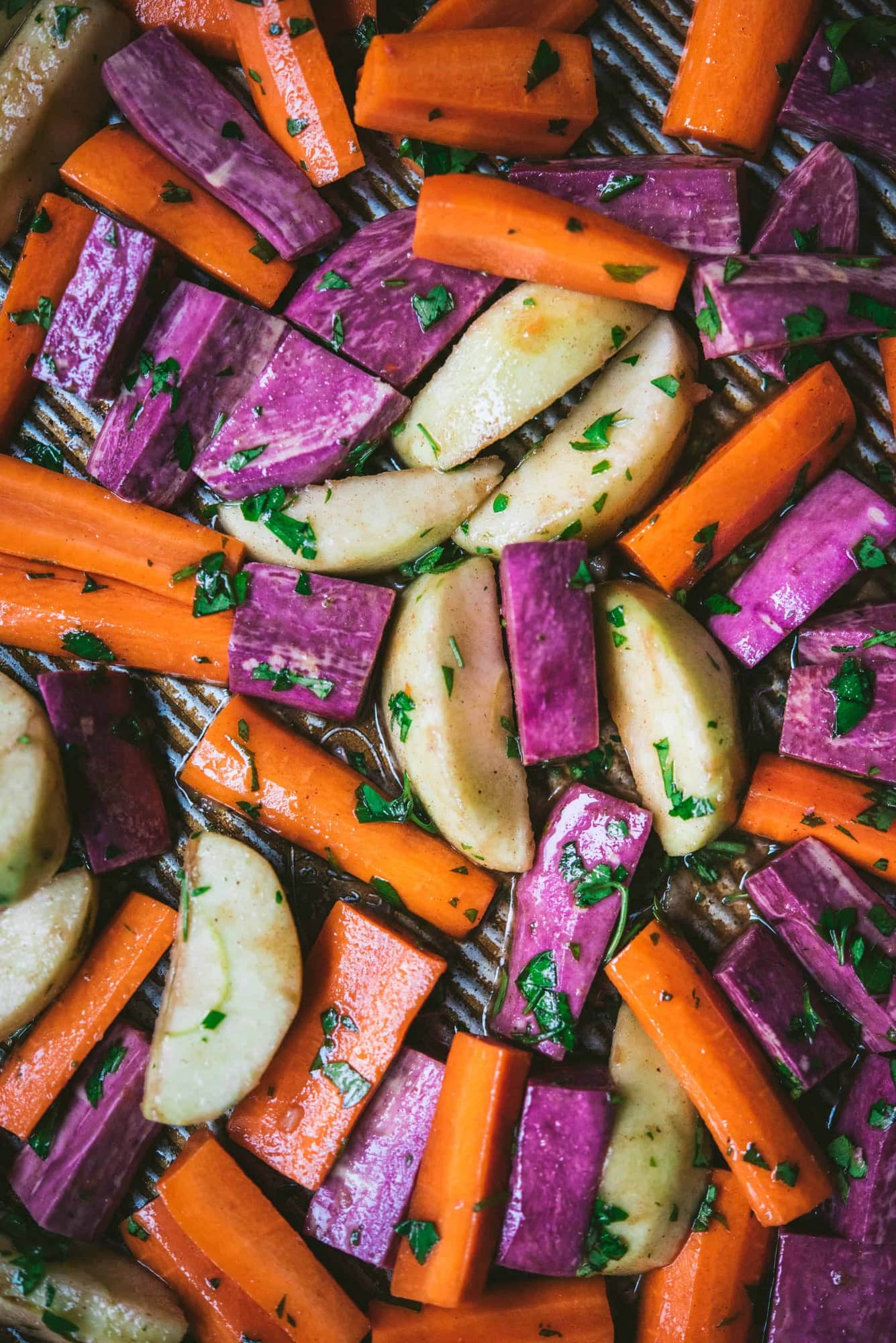 Close up of carrots, apples and purple sweet potatoes before roasting on baking sheet