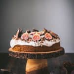 Side view of carrot cake with cream cheese frosting and fresh figs on a wooden cake stand
