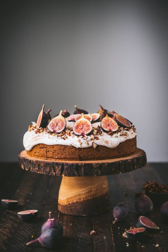 Side view of carrot cake with cream cheese frosting and fresh figs on a wooden cake stand