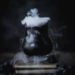 Black and purple halloween cocktail on a stack of old books with dry ice coming out of top