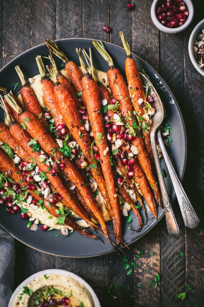 Close up of harissa roasted carrots over pumpkin hummus on a gray plate