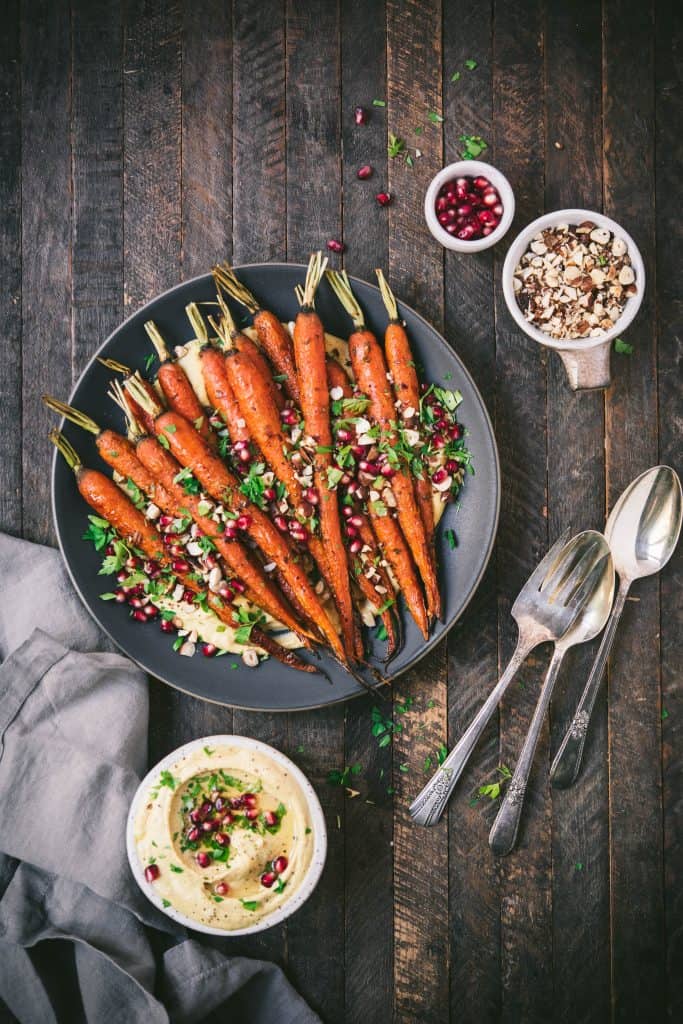 Overhead of harissa roasted carrots over a bed of creamy pumpkin hummus on a gray plate on wood background