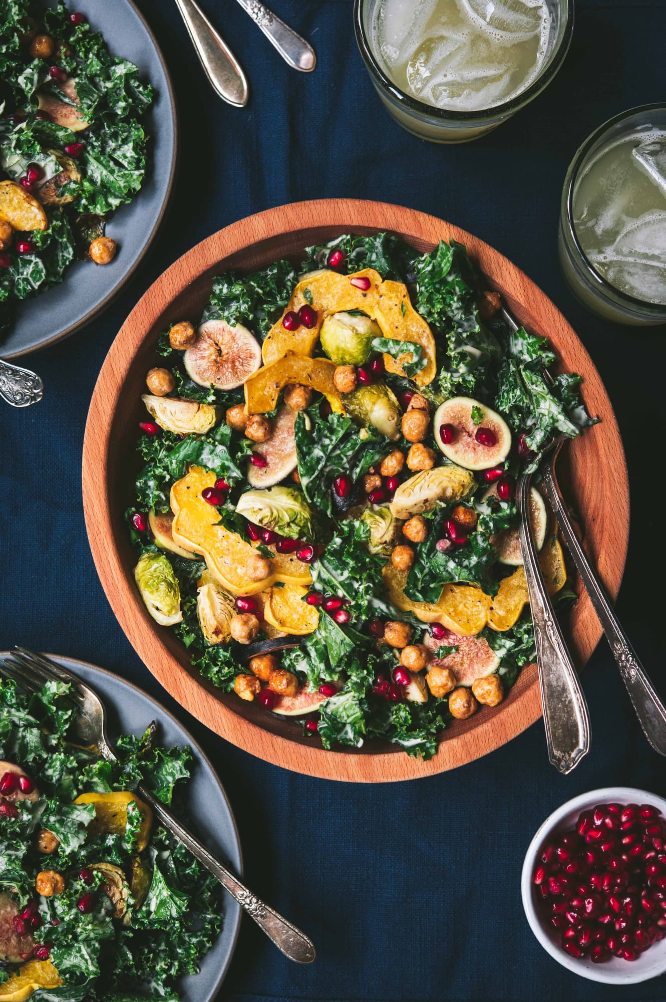 Large bowl of kale salad with fall roasted vegetables, tahini dressing and a bowl of pomegranate seeds