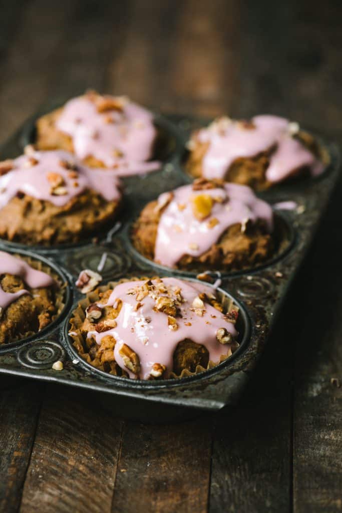 Side view of cranberry apple muffins with pink cranberry glaze in an antique muffin tray