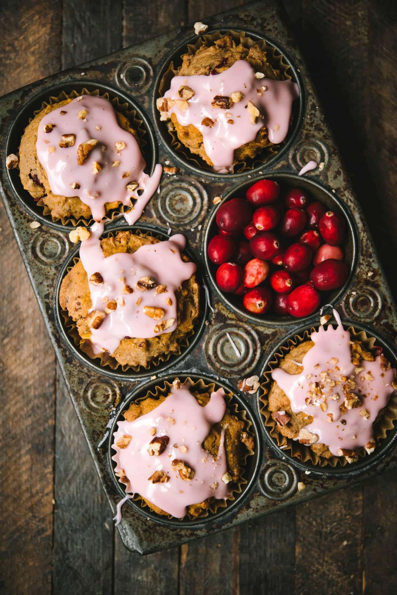 Overhead of cranberry apple muffins with pink cranberry glaze in an antique muffin tray