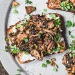 Close up of toast topped with ricotta, sauteed mushrooms and microgreens on a white plate