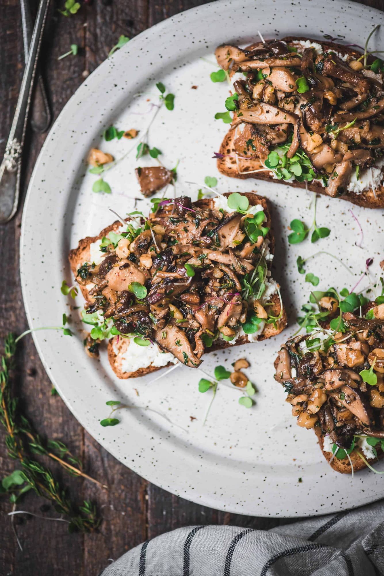 Toast topped with ricotta, sauteed mushrooms and microgreens on a white plate