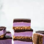 Stack of purple sweet potato cheesecake bars with chocolate ganache on white background